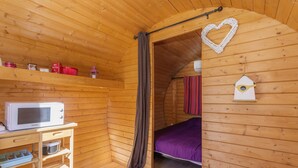A wooden cabin interior with a bed, a microwave, and a shelf with items. - Barrel Violet Apartment with Mountain View, Wi-Fi, and Air Conditioning (Saint-André)
