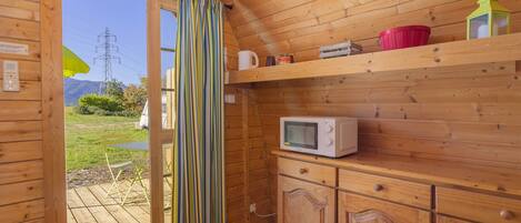 A wooden cabin interior with a kitchen area, including a microwave, cabinets, and a window with curtains.