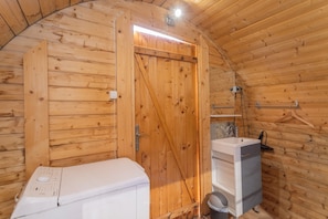 Interno di una baita in legno con lavatrice, lavandino e una porta.