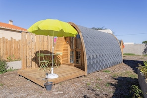 A small wooden structure with a curved roof, a wooden deck, and a green umbrella. - Pod Anis Cabin with Air Conditioning (Saint Andre)