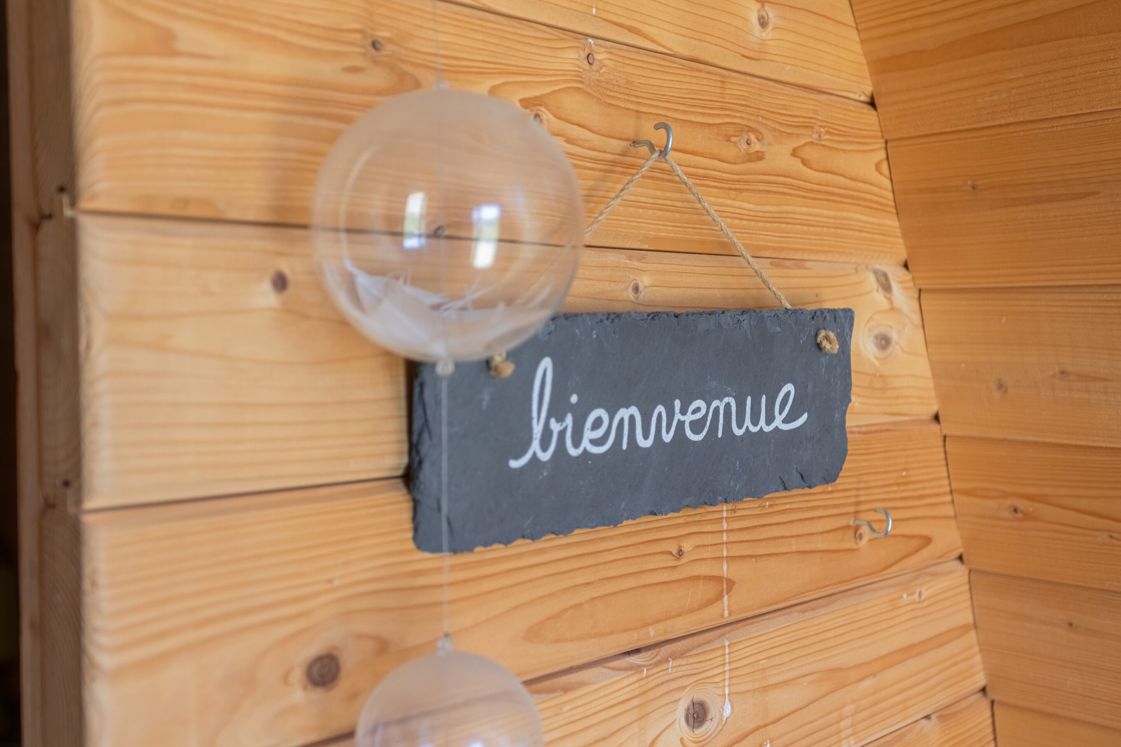 Un mur en bois sur lequel est accrochée une enseigne portant l’inscription « bienvenue » et deux décorations en verre suspendues.