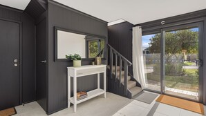 A modern entryway with a dark wood door, a white console table with a mirror, and a glass door leading to a garden.