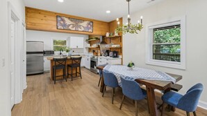 A modern kitchen with a wooden ceiling, a dining area with blue chairs, and a large window with blinds.