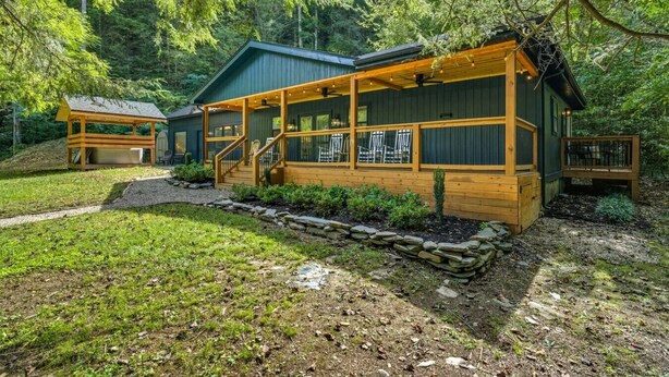 A cabin with a covered porch, stone retaining wall, and a small deck.