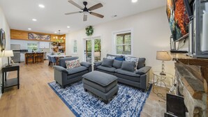 A spacious living room with a gray sectional sofa, a dining area with a kitchen in the background, and a fireplace with a TV.