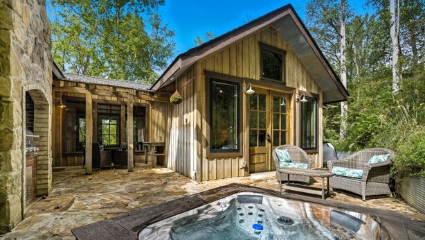 Een rustieke hut met een stenen terras, een hottub, rieten meubels en een stenen openhaard.