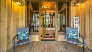 Een houten interieur met twee rieten stoelen met bloemenkussens, een houten deur en een bordje met de tekst 'WELL'.