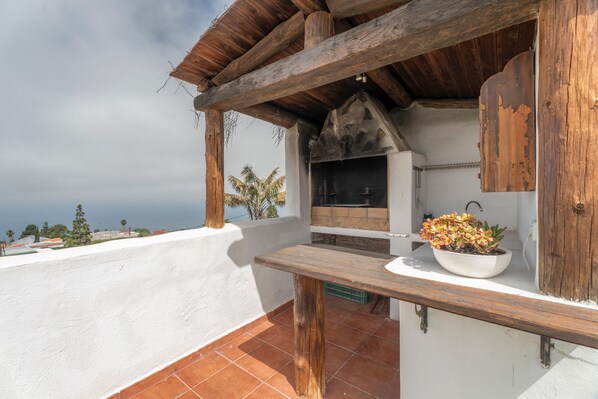 A wooden pergola with a grill, a white wall, and a potted plant on a terrace.