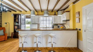 A kitchen with a central island, bar stools, pendant lights, and a wooden ceiling.