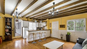 A spacious living area with a wooden floor, a white sofa, a coffee table, and a kitchen with white cabinets and bar stools. - Vacation Home 'La Era' with Mountain View, Private Pool and Wi-Fi (Adeje)