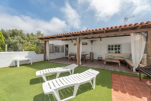 A patio with two white lounge chairs, a wooden table, and a sofa with a canopy.