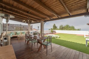An outdoor patio with a wooden deck, a dining table with chairs, a sofa with cushions, and a view of a green lawn and trees. - Vacation Home 'La Era' with Mountain View, Private Pool and Wi-Fi (Adeje)