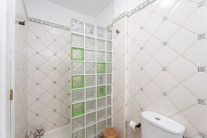 Une salle de bain avec un mur carrelé, des toilettes et un espace douche.