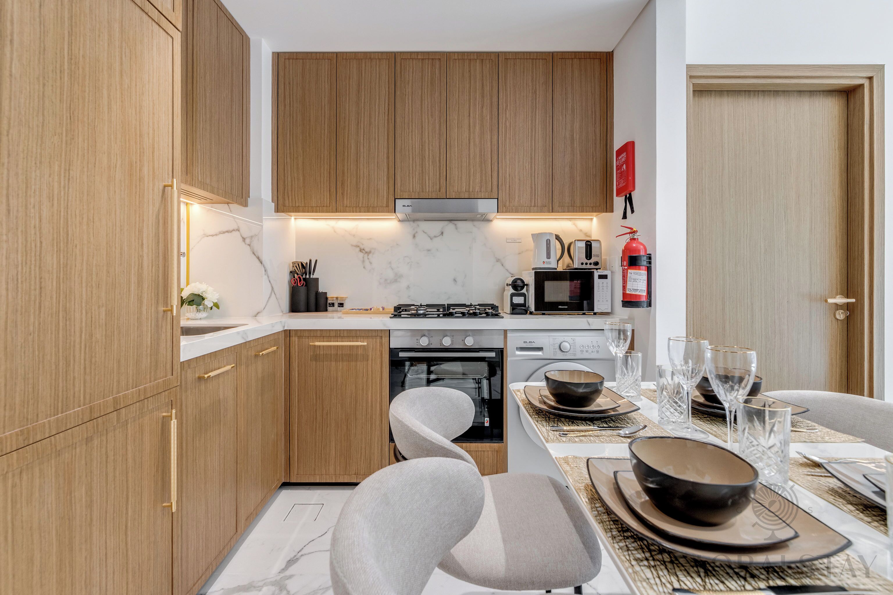 A modern kitchen with wooden cabinets, a gas stove, an oven, and a microwave. There is a dining table set with plates, bowls, and glasses.