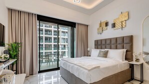 A modern bedroom with a large bed, a desk with a chair, and a balcony with a view of buildings.