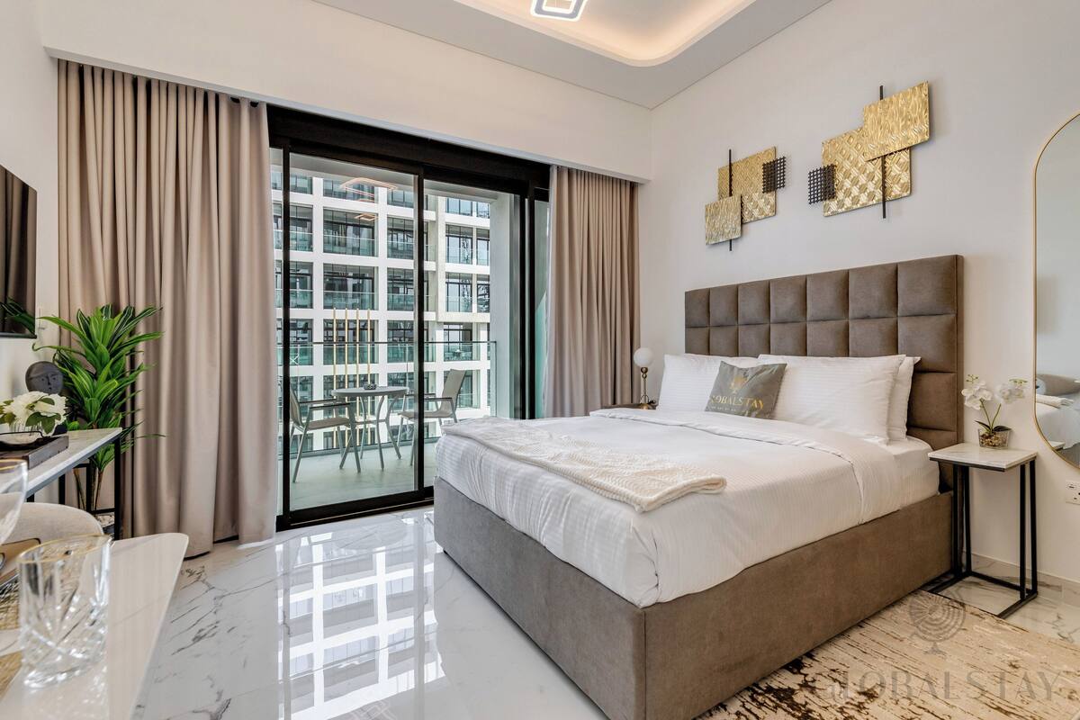 Un dormitorio moderno con una cama grande, un escritorio con una silla y un balcón con vistas a edificios.