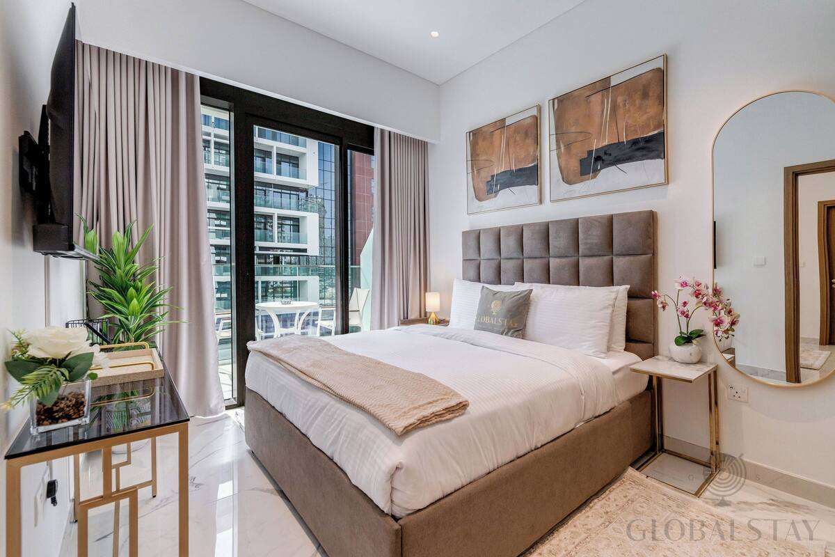 Un dormitorio moderno con una cama grande, un televisor montado en la pared, una ventana con cortinas y vistas al balcón.