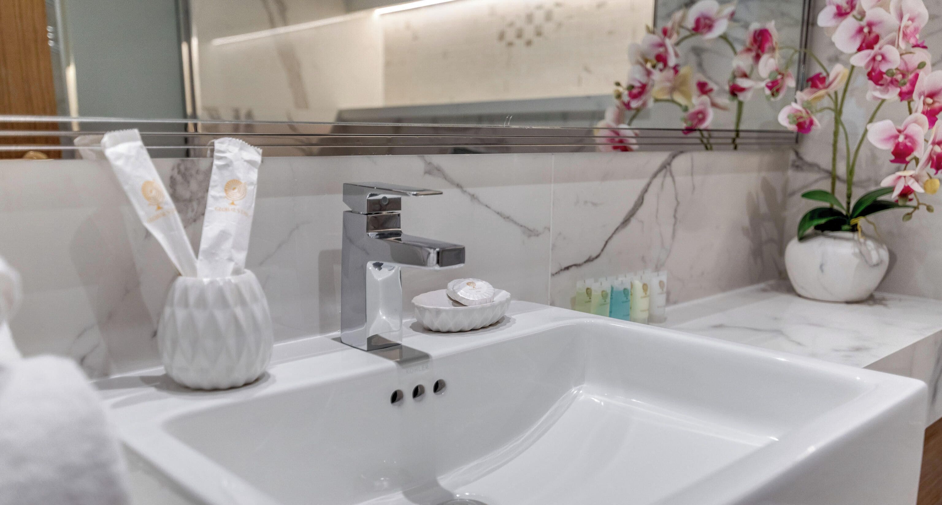Un baño moderno con lavamanos blanco, grifo cromado y salpicadero de mármol.