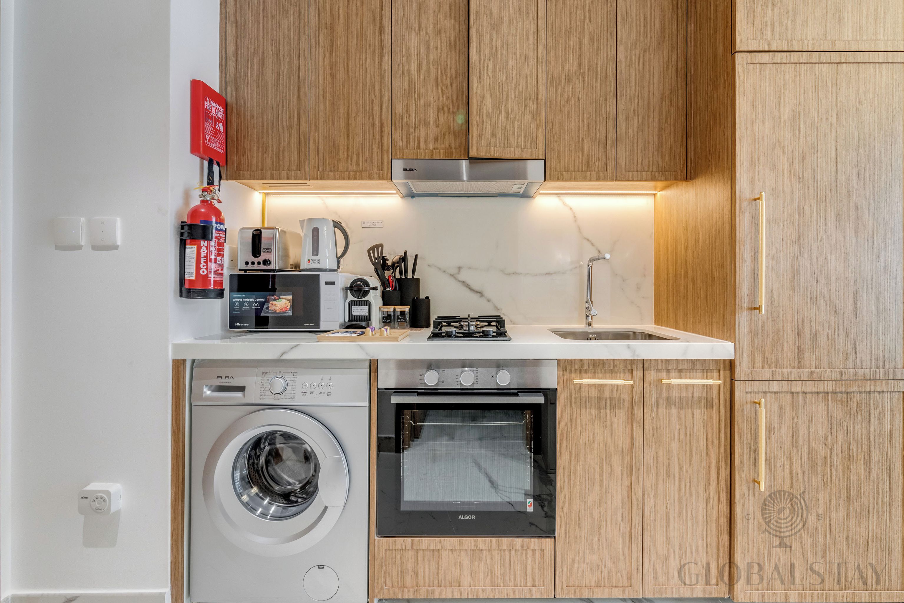 Eine kleine Küche mit Waschmaschine, Backofen und Kaffeemaschine.