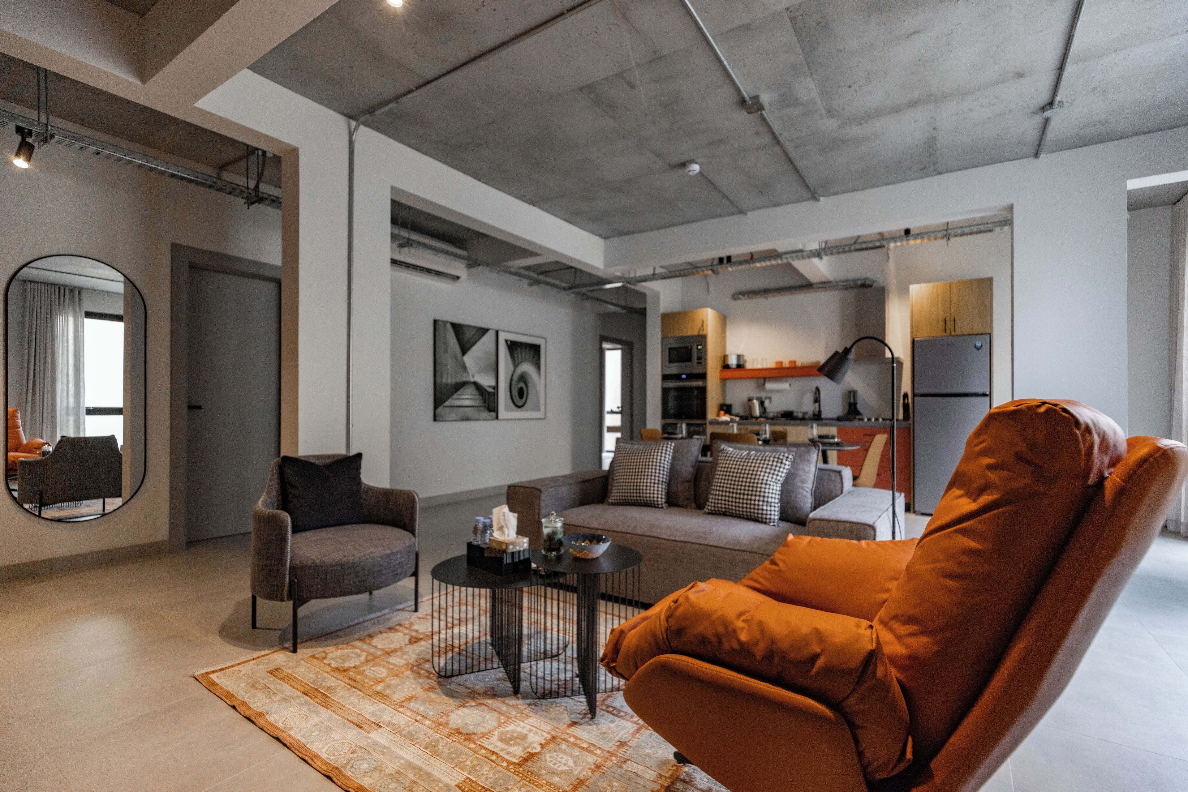 A modern living room with a sofa, armchair, and a coffee table. There is a kitchen area with appliances visible in the background.