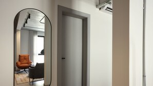 A modern hallway with a large mirror, a closed door, and a seating area with a chair and table. - C LIVING 3 - ALMALQA (Riyadh)