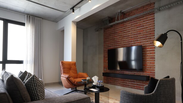 A modern living room with a sofa, armchairs, a coffee table, and a flat-screen TV mounted on a brick wall. - C LIVING 3 - ALMALQA (Riyadh)