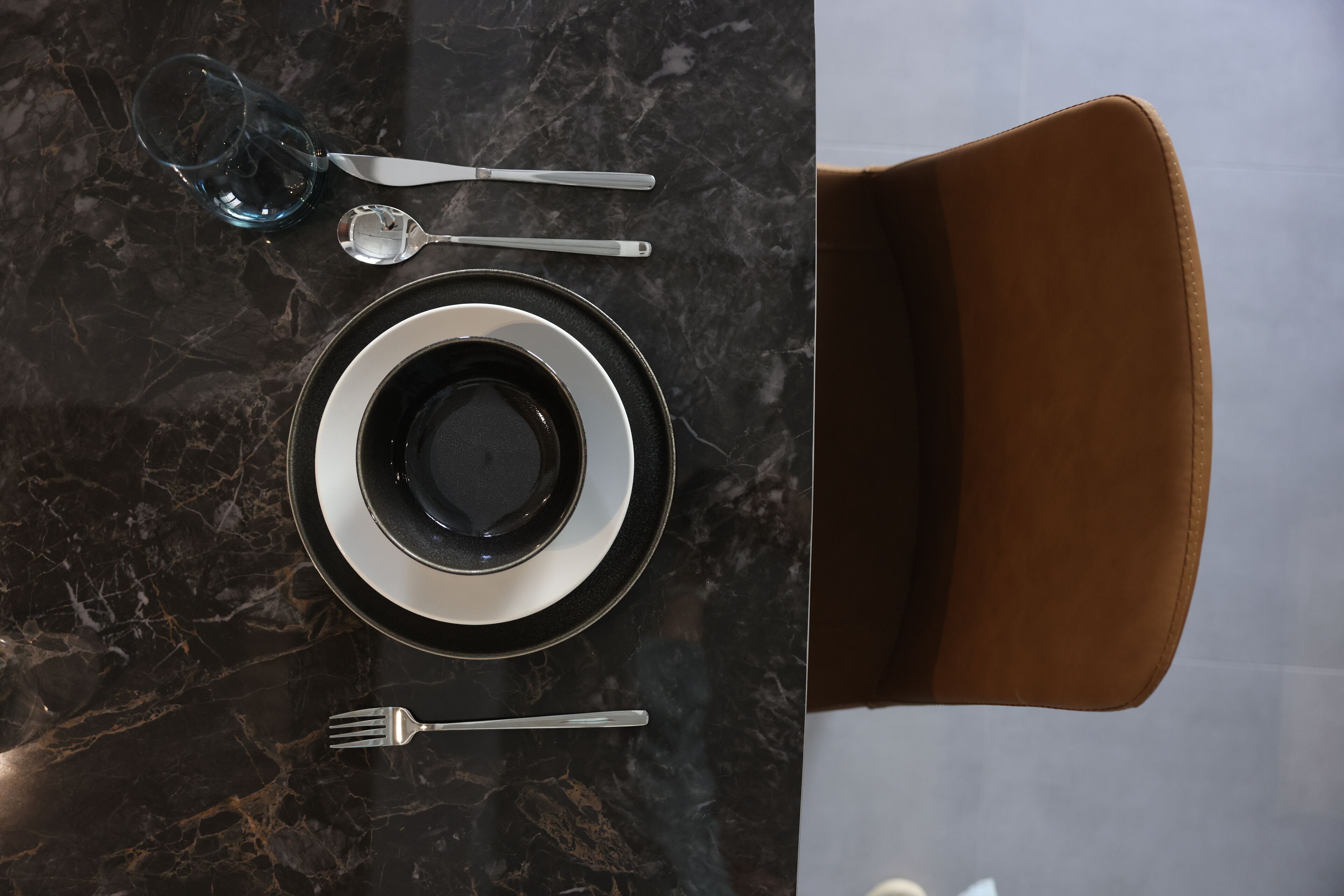A dining table with a black marble top, a brown leather chair, and a glass of water.