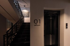 A modern interior with a staircase, a wall-mounted elevator sign, and a patterned wall decoration. - C LIVING 3 - ALMALQA (Riyadh)