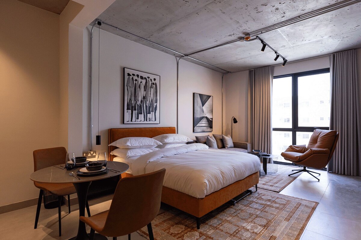 Une chambre d’hôtel moderne dotée d’un grand lit, d’une table à manger, d’une chaise et offrant une vue sur la ville grâce à de grandes fenêtres.
