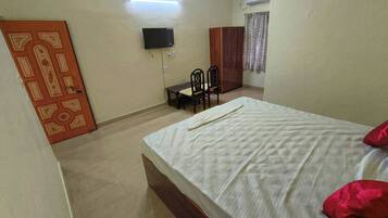 A bedroom with a bed, a TV mounted on the wall, a wardrobe, and a desk with chairs.
