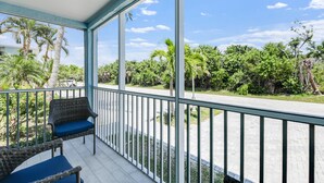 A balcony with wicker chairs and a view of a road and greenery.