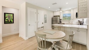 A modern kitchen with white cabinets, a stainless steel refrigerator, and a dining area with a round table and chairs.