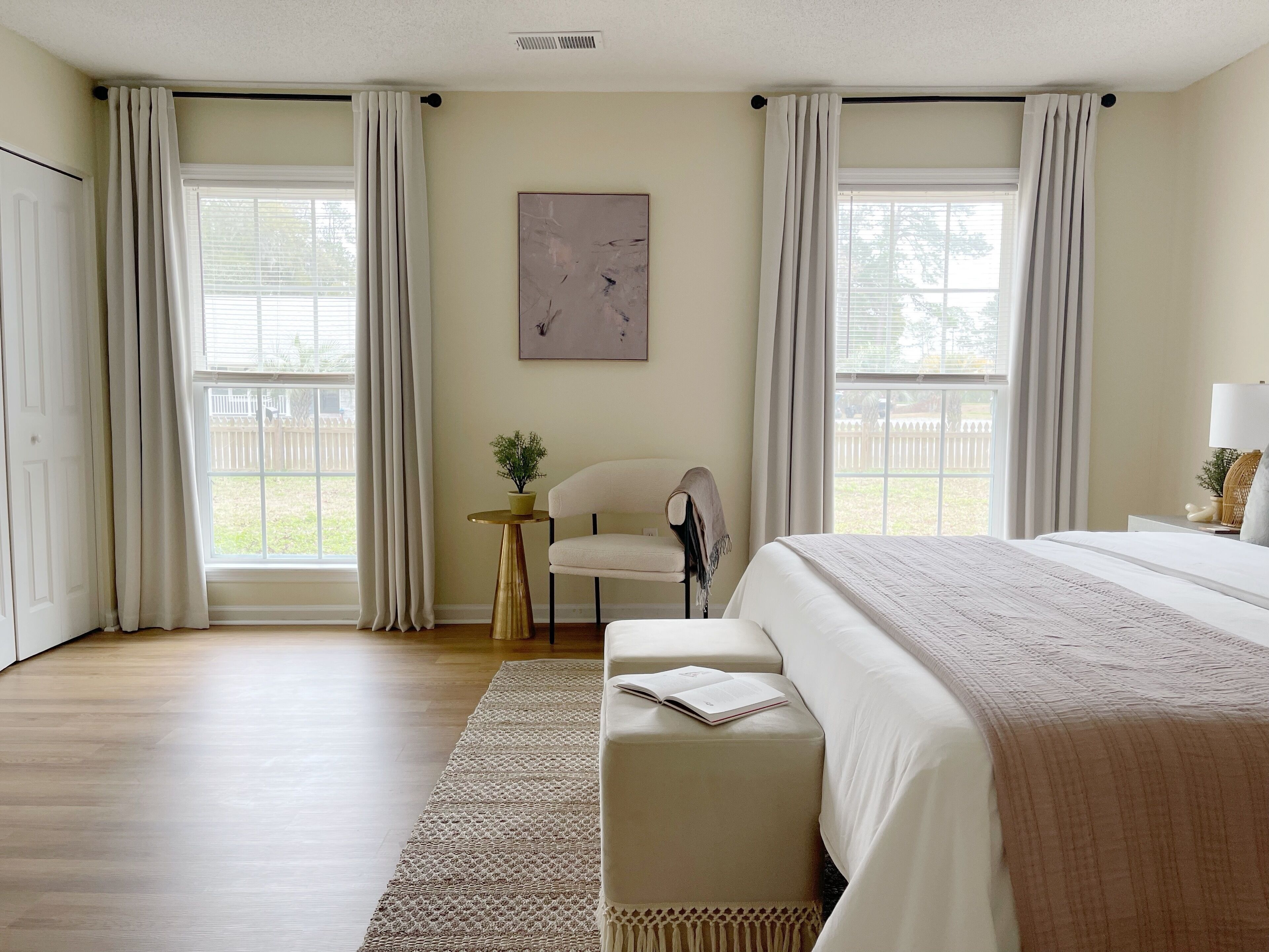 A bedroom with a large bed, a chair, a small table with a plant, and a painting on the wall.
