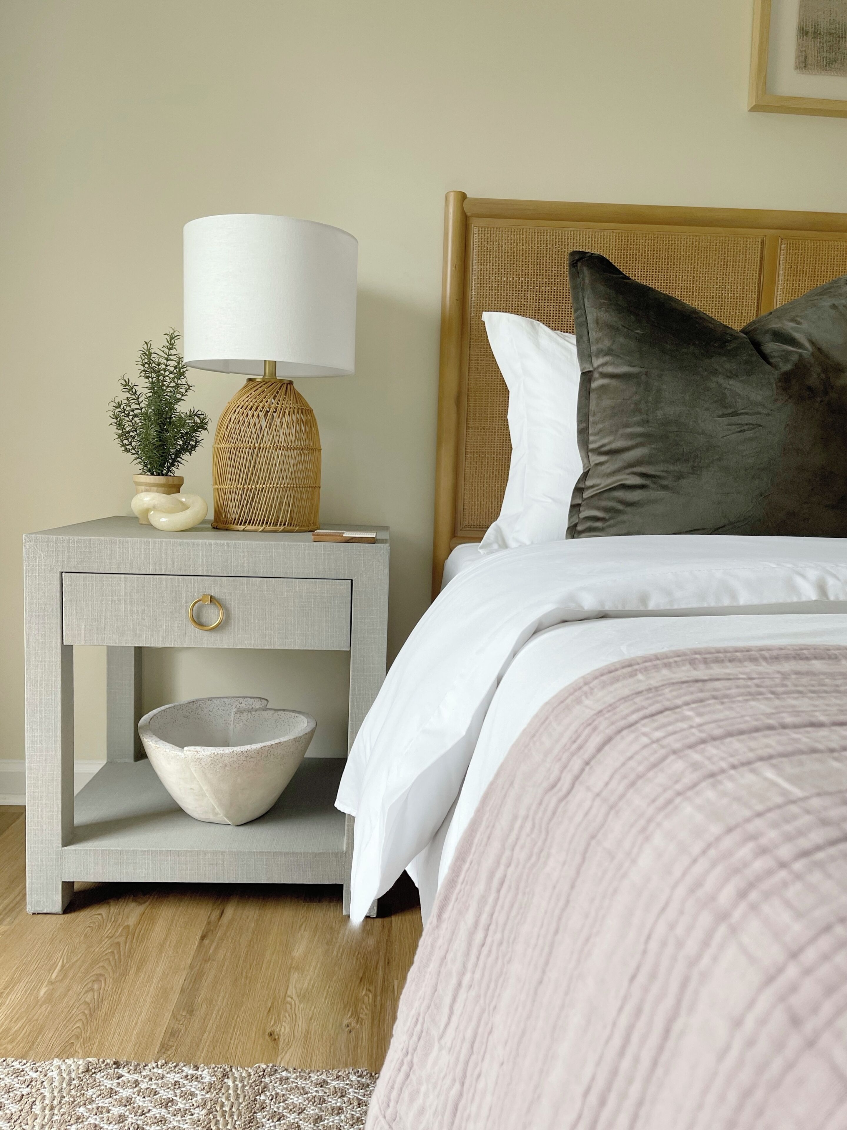 Une chambre à coucher bien rangée, avec un lit, une table de chevet sur laquelle se trouve une lampe, un bol et une petite plante en pot.
