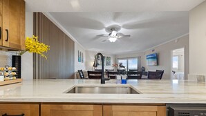 A modern kitchen with a central island, wooden cabinets, and a ceiling fan. - Top Floor 3BR | Panoramic Gulf & Seabird Sanctuary | Pool, Hot Tub, Sleeps 11 (Indian Shores)