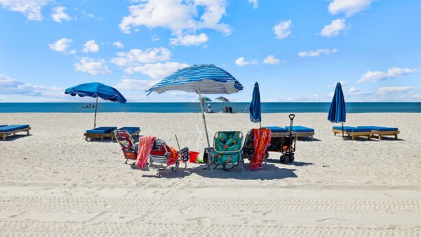 A beach with several sun loungers and umbrellas, a beach chair, and a beach cart. - Top Floor 3BR | Panoramic Gulf & Seabird Sanctuary | Pool, Hot Tub, Sleeps 11 (Indian Shores)