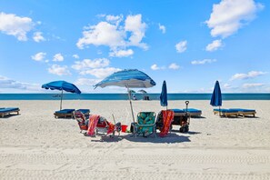 A beach with several sun loungers and umbrellas, a beach chair, and a beach cart.