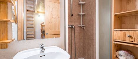 A bathroom with a white sink, wooden shelves, a shower with a glass door, and a wooden cabinet.