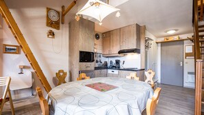 Une cuisine chaleureuse avec des meubles en bois, une table à manger recouverte d’une nappe à motifs et une chaise en bois avec une découpe en forme de cœur.