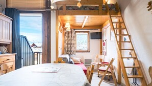 Une pièce confortable avec un lit, un bureau, une chaise, une échelle et une fenêtre donnant sur un paysage enneigé.