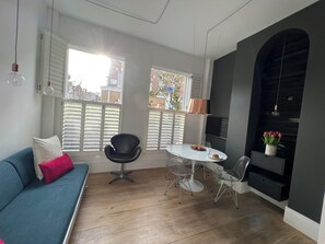 A modern living room with a blue sofa, a black chair, a round dining table, and a TV mounted on a dark wall. - Queen's Park Small & Perfect (London)