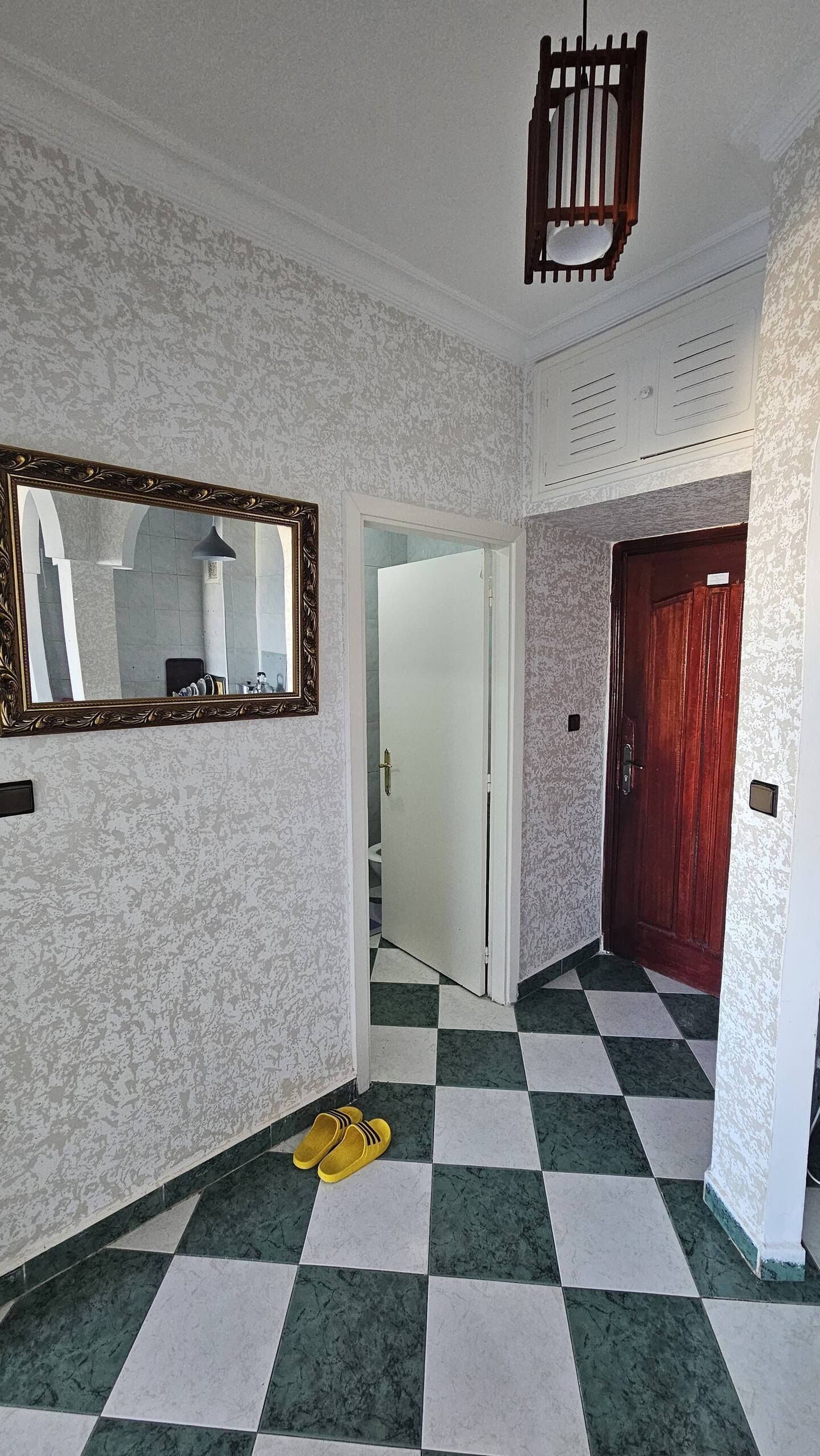 Un pasillo con piso a cuadros, un espejo con marco ornamentado y una puerta con panel de madera.