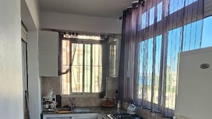 A kitchen with white cabinets, a granite countertop, a window with curtains, and a tiled floor. - Brise d’Océan Tanger (Tangier)