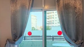 A bedroom with a bed, curtains, and a view of an outdoor balcony with a table and chairs.