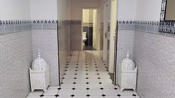 A hallway with patterned walls and a tiled floor, leading to a bathroom with a toilet and a mirror.