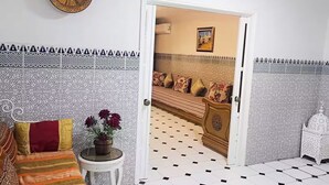 A room with a patterned floor, a sofa with cushions, a small table with a plant, and a decorative plate on the wall.
