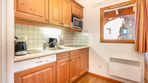 A compact kitchen with wooden cabinets, a microwave, a coffee maker, and a dishwasher. - Charming apartment, sleeps 6, balcony (Modane)