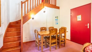 A staircase leading to a room with a wooden table and chairs, a red door, and a bulletin board on the wall. - Charming apartment, sleeps 6, balcony (Modane)