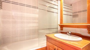 A bathroom with a glass shower enclosure, a white sink, and a wooden vanity. - Charming apartment, sleeps 6, balcony (Modane)