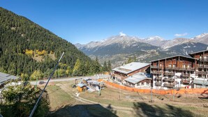 Un chalet de montagne doté de plusieurs balcons, d’un télésiège et offrant une vue sur la forêt et les montagnes environnantes.